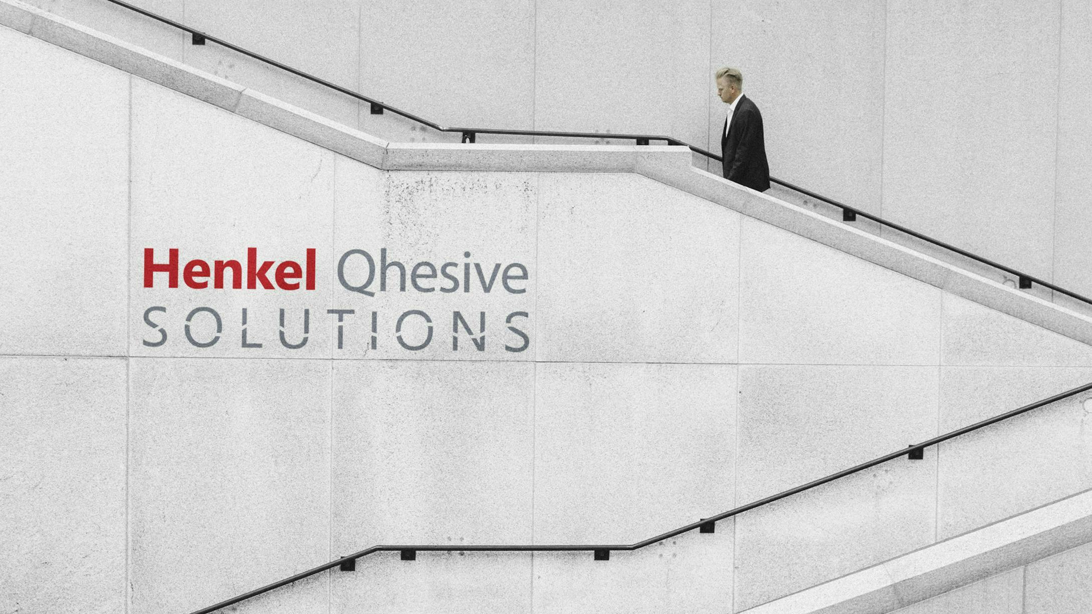 A man walking up stairs with Henkel Qhesive Solutions logo on the wall